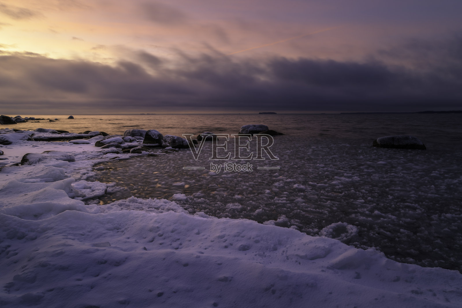 美丽的日落时分，冰雪覆盖在海岸边的岩石上照片摄影图片