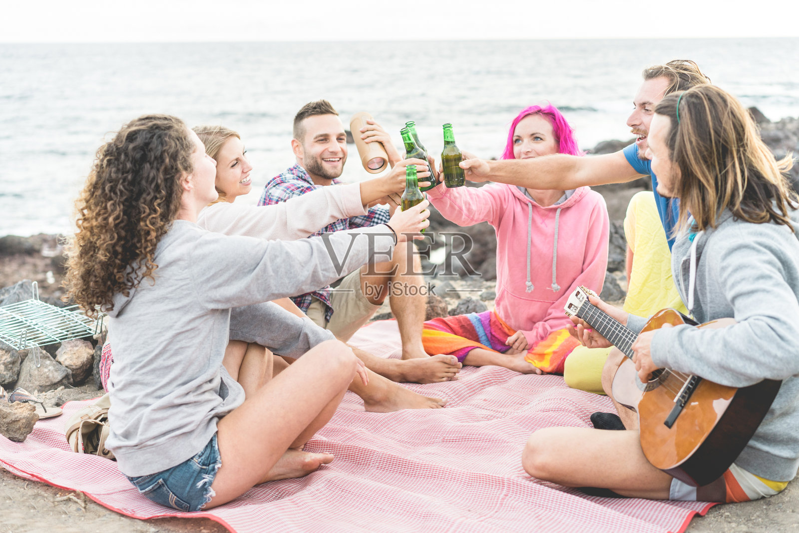 快乐的朋友欢呼与啤酒和演奏音乐在露营户外-时髦的人有乐趣在一起野餐-友谊，青年生活方式和度假概念-专注于手瓶照片摄影图片