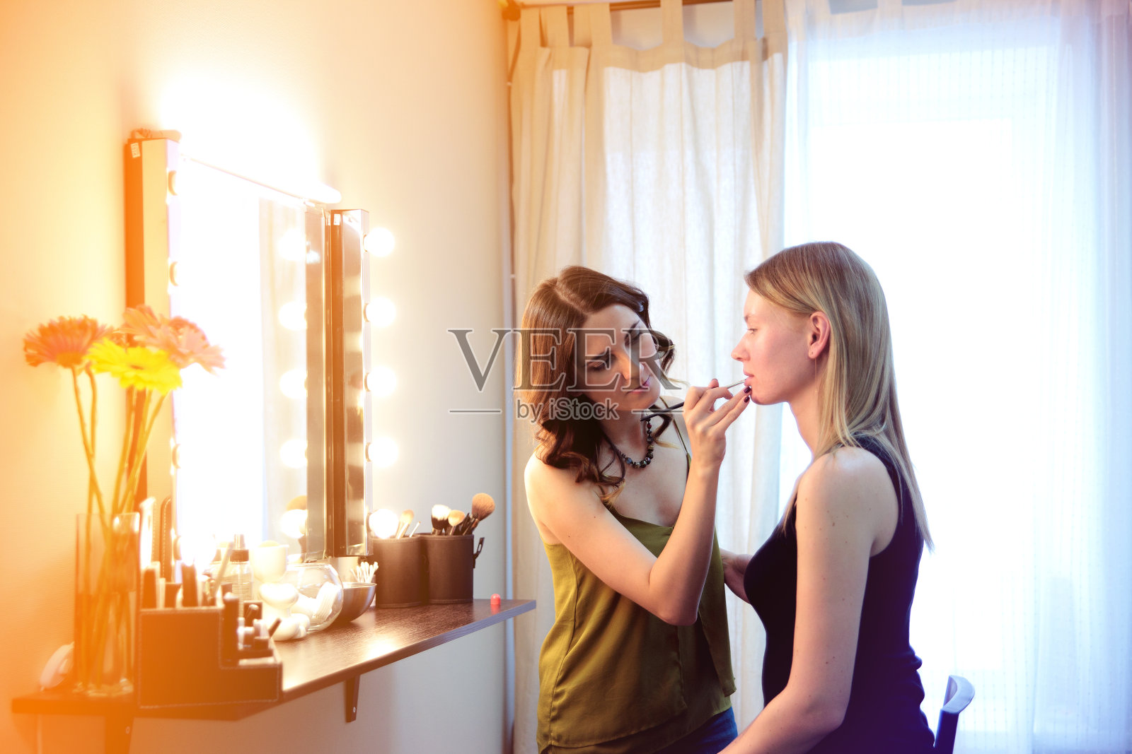 化妆师在美容工作室用刷子化妆迷人的金发女孩。照片摄影图片