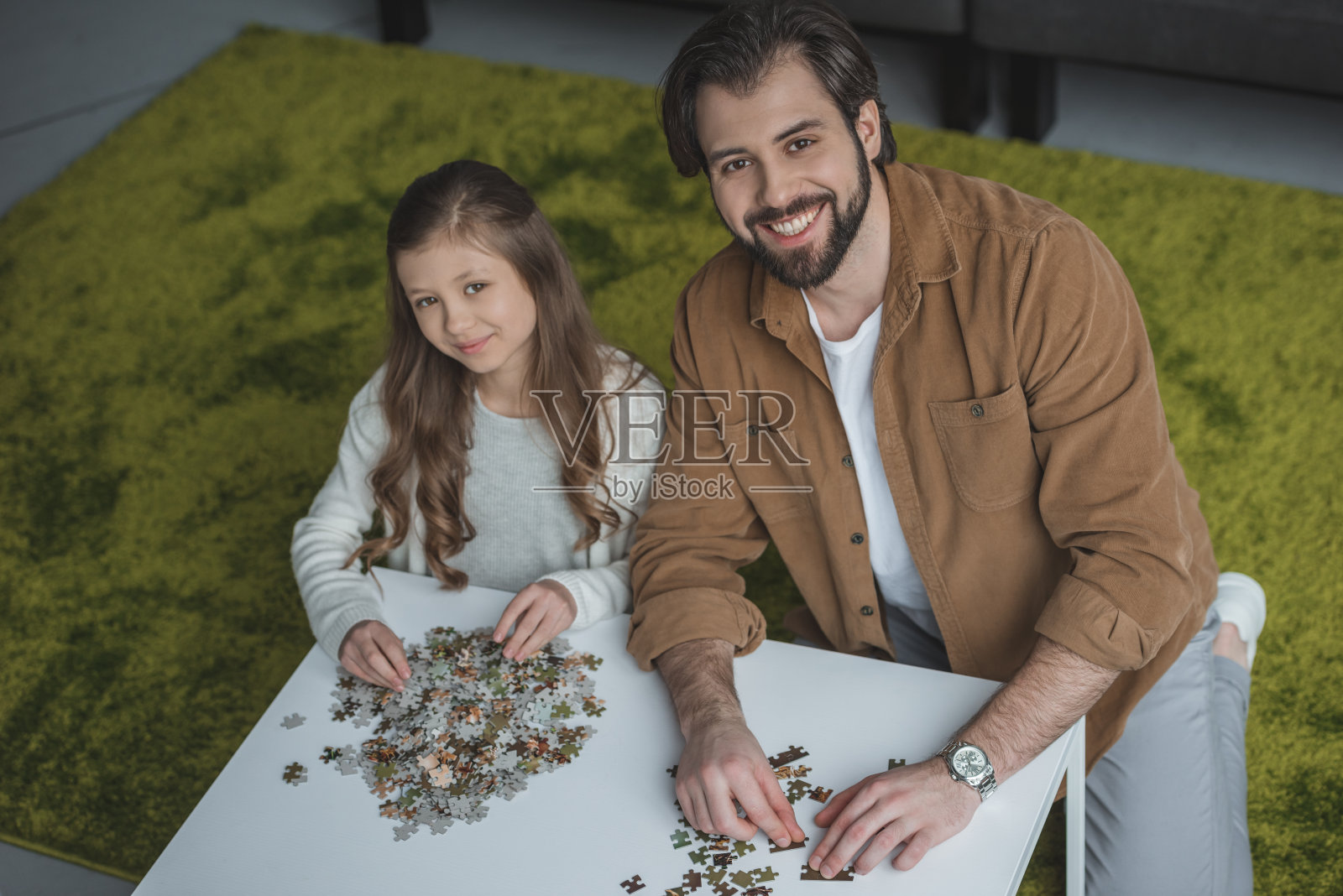 高角度的父亲和女儿坐在桌子上拼图块和看相机照片摄影图片