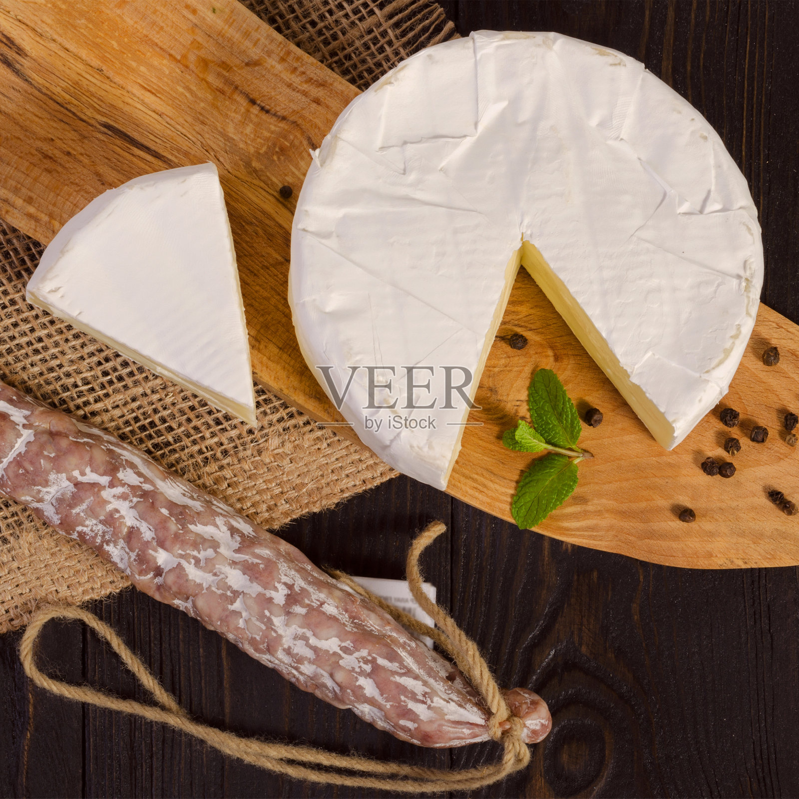 圆的卡芒贝尔奶酪，切片，放在木板上，fuet香肠，放在木板上，带袋子。卡门贝尔奶酪是一种用牛奶制成的软脂肪奶酪。照片摄影图片