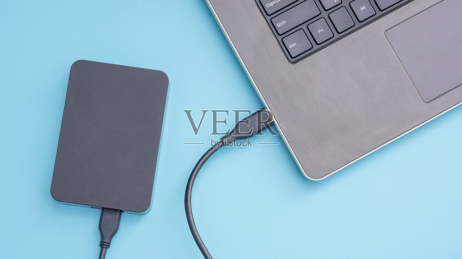 黑色外接硬盘连接到蓝色背景的笔记本电脑。照片摄影图片