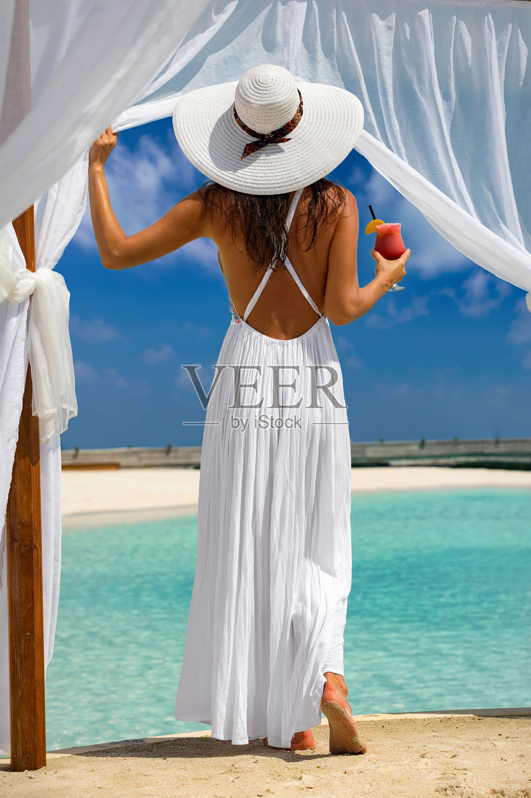 女人享受热带海滩的景色与饮料在她的手照片摄影图片