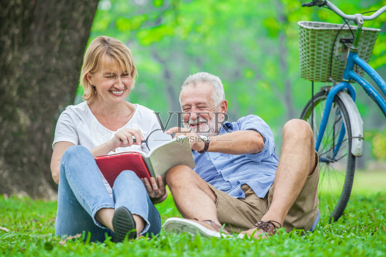 快乐的老夫妻带着笑脸一起享受，用放大镜在公园看书，花时间和放松时间的概念。照片摄影图片