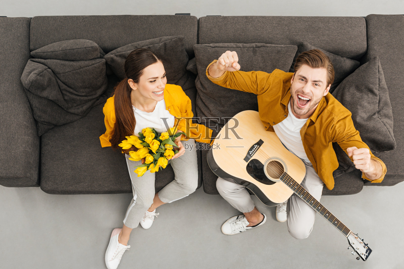 头顶上的男人举着吉他举起拳头大喊，而他的女朋友在家里的沙发上捧着花束照片摄影图片