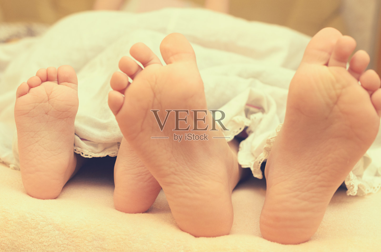 宝宝的脚从床上的毯子下面伸出来。照片摄影图片