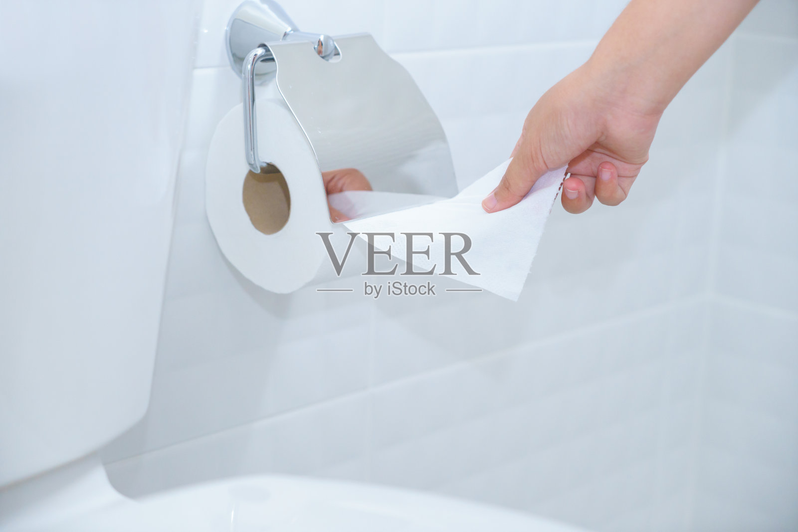 一个女人的手在白色和干净的厕所使用卫生纸的特写。照片摄影图片