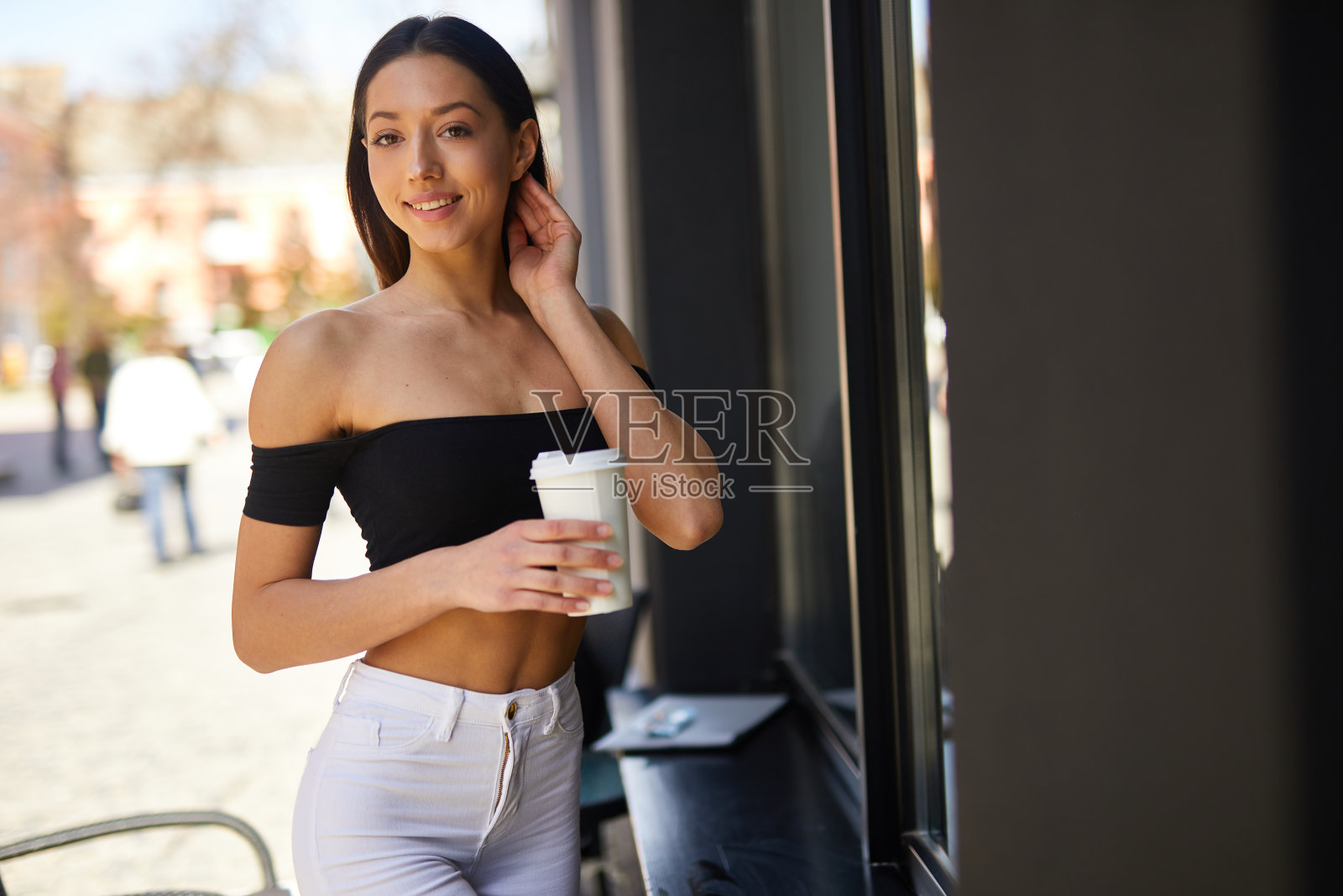 黑发女孩站在街上看着镜头，喝着白色杯子里的美味咖啡，拍摄春天的照片照片摄影图片