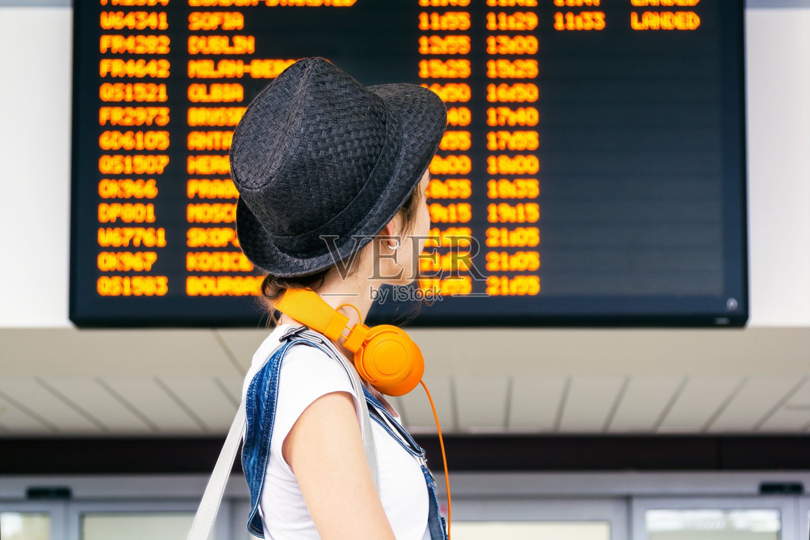 年轻的时髦女孩旅行者在国际机场看航班信息板，查看她的航班。照片摄影图片