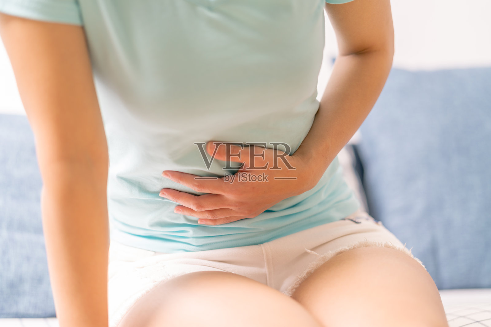 年轻女子坐在沙发上腹痛，胃疼，是经前综合症的症状照片摄影图片