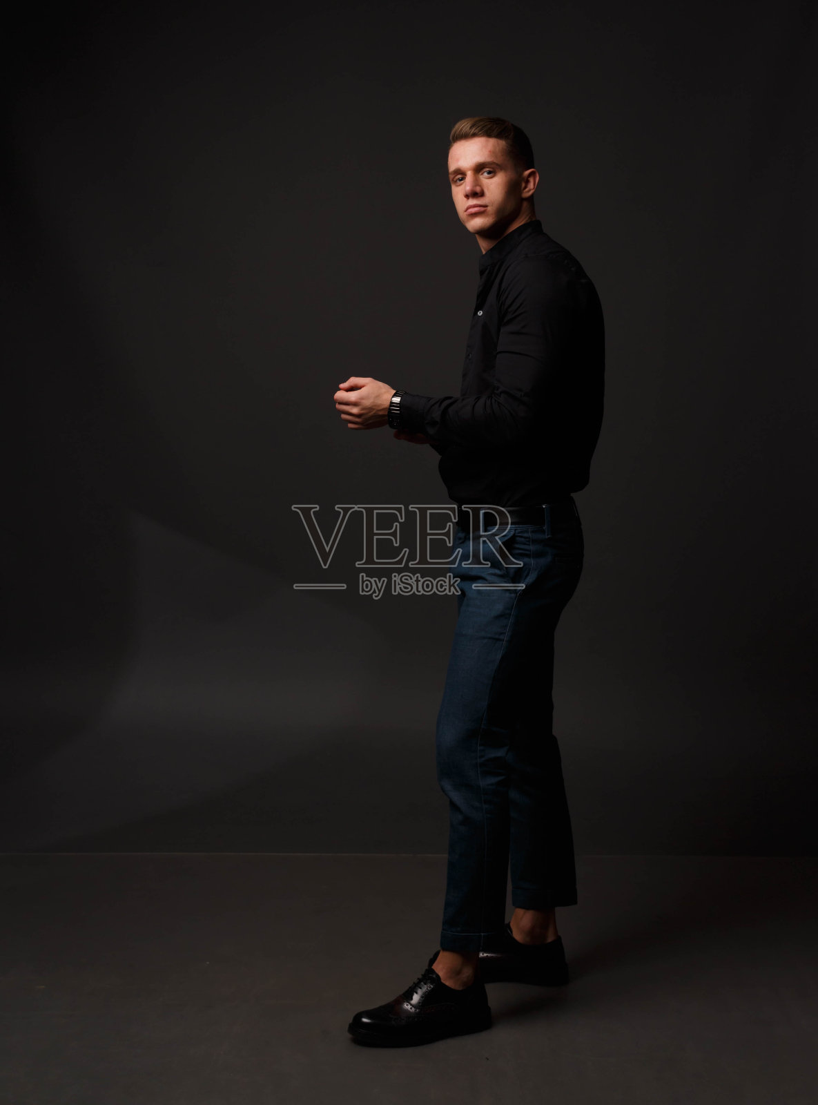 一个穿着黑色衬衫和蓝色裤子的有魅力的白人男子站在黑暗的背景上照片摄影图片