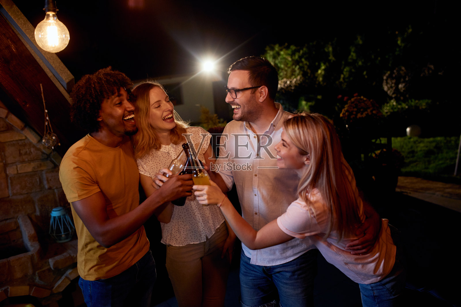愉快的朋友们晚上在露台上举行饮酒聚会。照片摄影图片