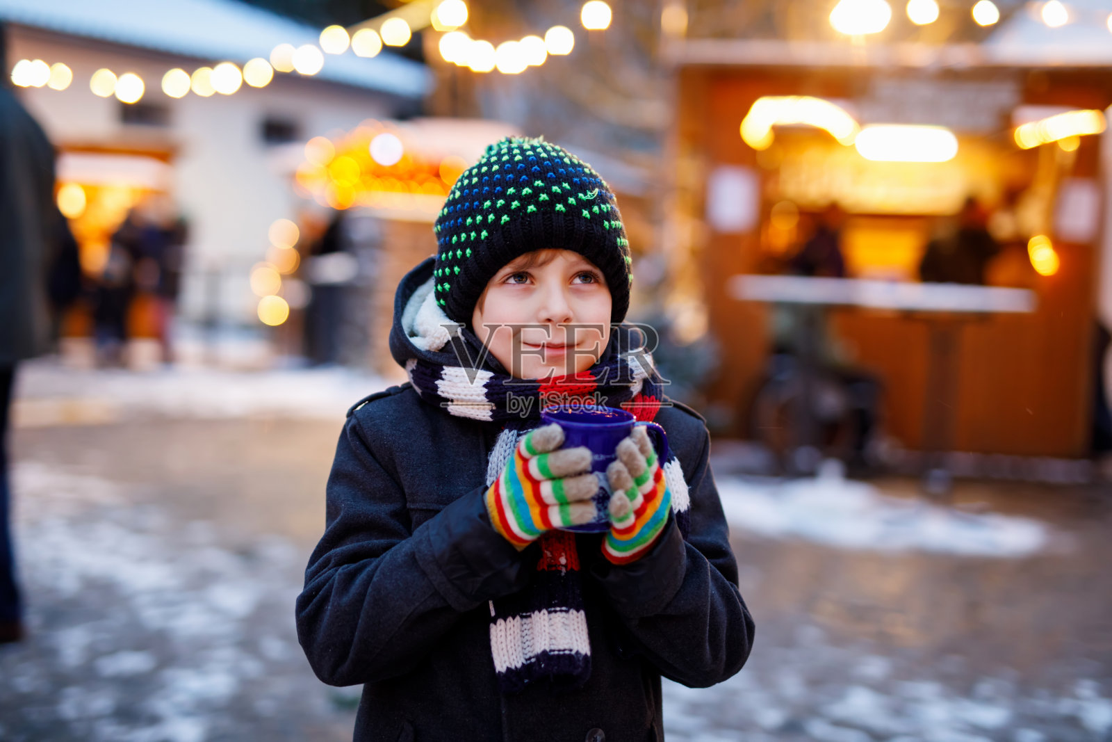 可爱的小男孩喝热儿童潘趣酒或巧克力在德国圣诞市场。德国传统家庭市场上快乐的孩子，穿着五颜六色冬装的笑男孩照片摄影图片