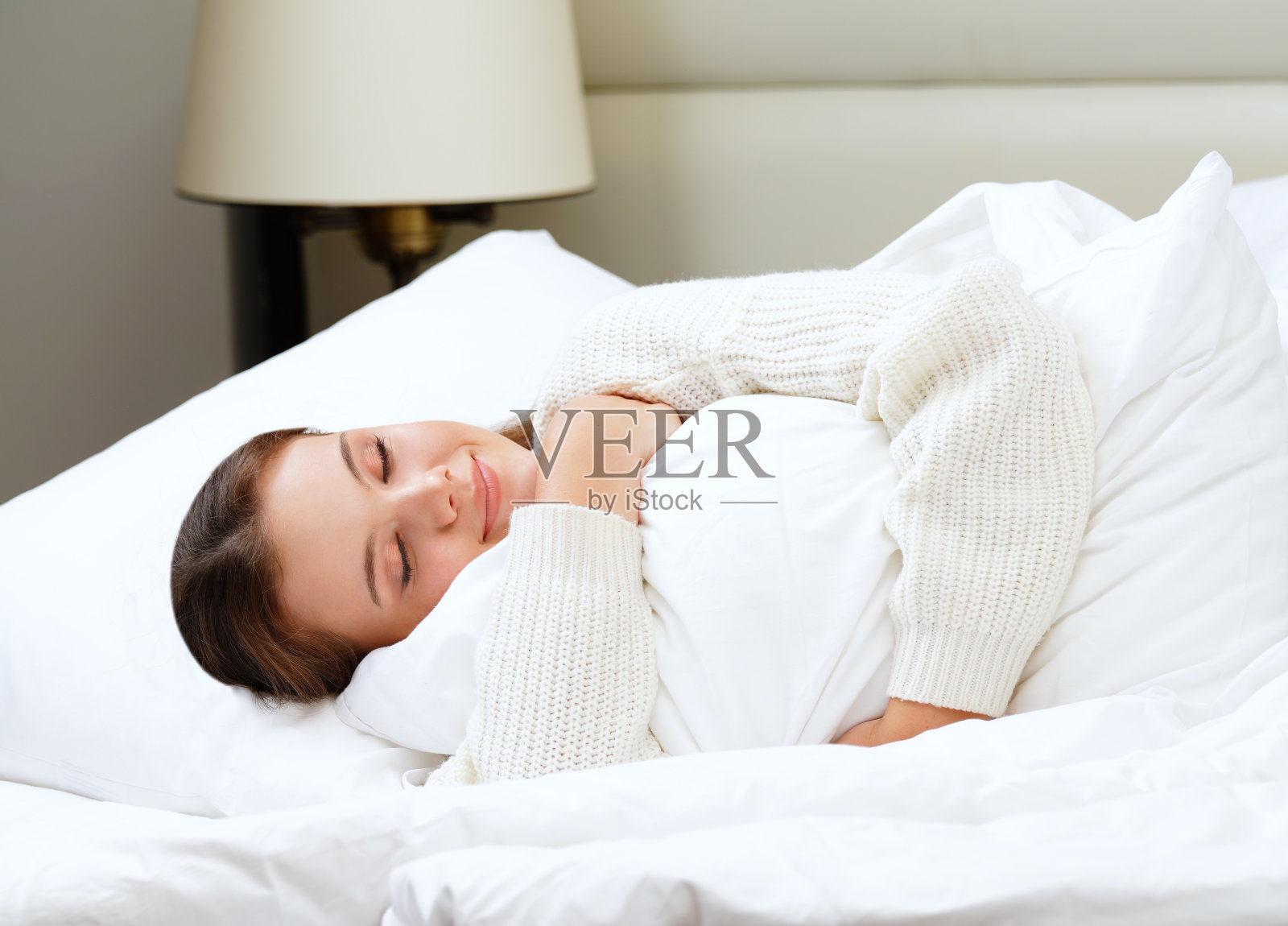 美丽迷人的年轻白种女子黑发早上躺在白色的床上抱着枕头睡觉照片摄影图片
