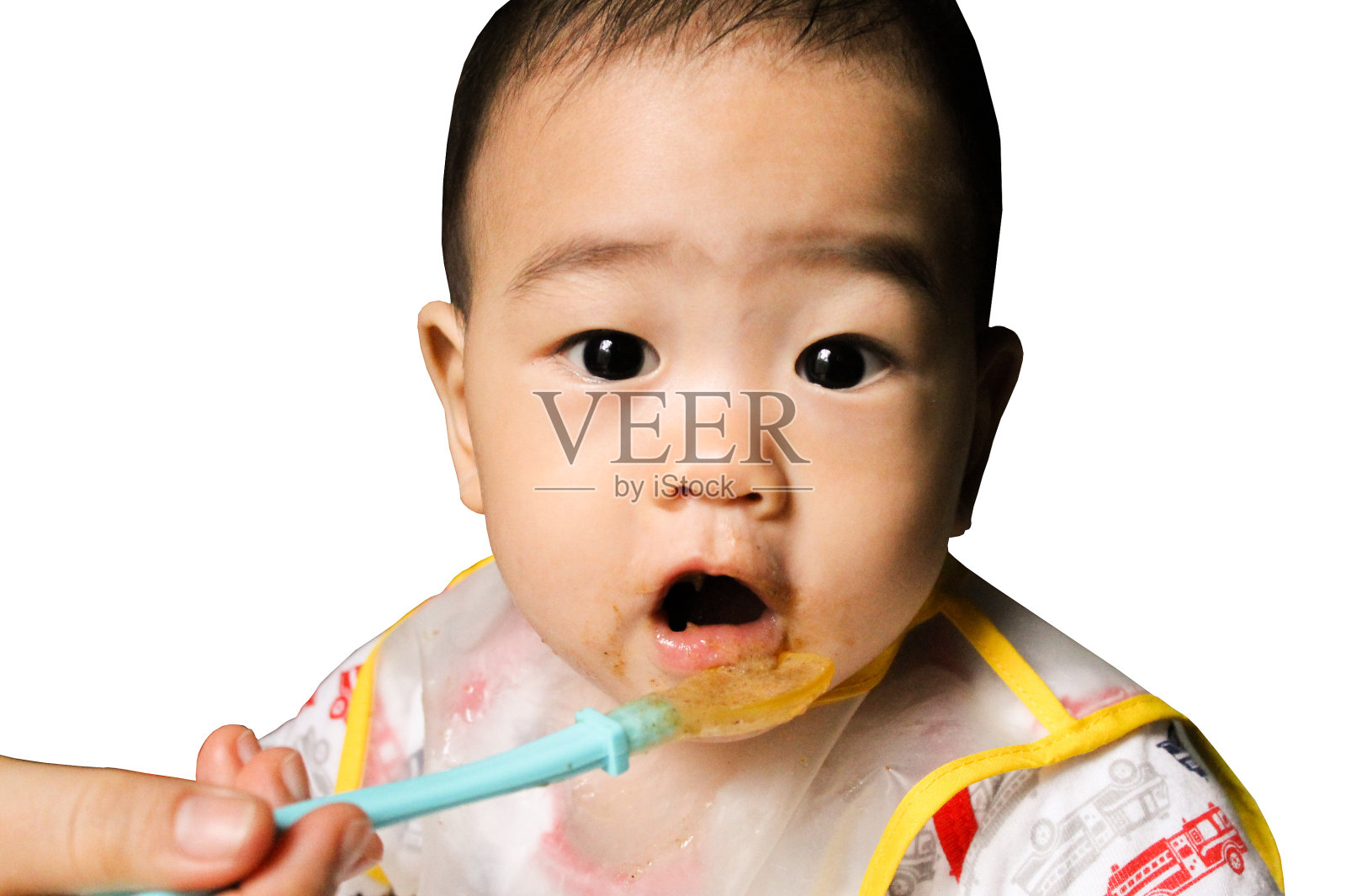 近距离观察快乐的小7个月大的儿子在看通过塑料围嘴吃在椅子上的婴儿后，妈妈让他吃鳄梨和香蕉混合。快乐的孩子的脸。亚洲婴儿张着嘴。照片摄影图片