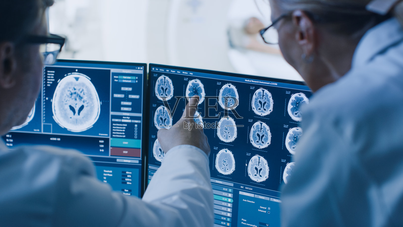 在控制室，医生和放射科医生讨论诊断，同时观看程序和显示器显示的大脑扫描结果，在背景患者接受MRI或CT扫描程序。照片摄影图片