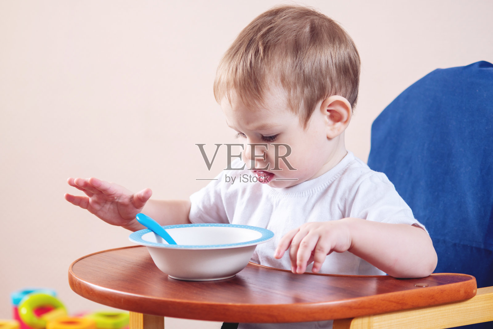 小男孩学着在儿童餐桌上吃饭，研究厨房里的盘子和勺子照片摄影图片