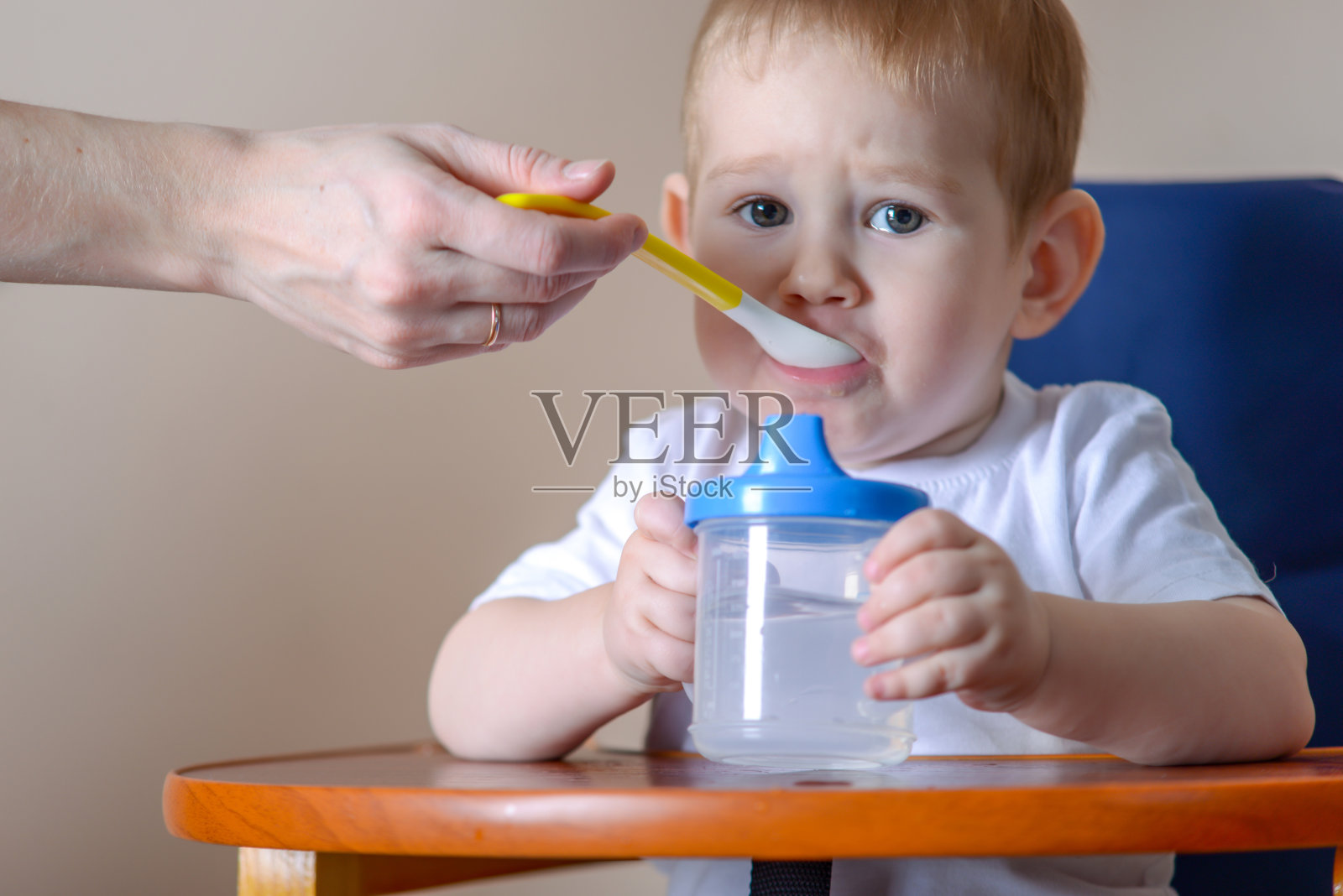 小男孩学着在厨房里孩子们的餐桌上吃饭。母亲手里拿着一勺粥喂孩子照片摄影图片