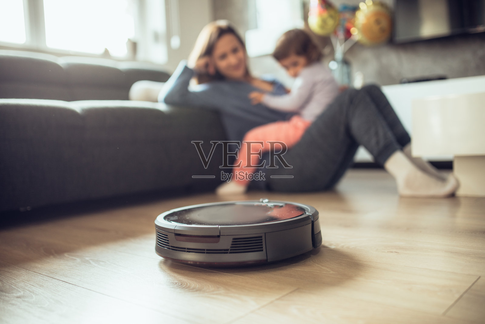 当妈妈和女儿一起放松的时候，机器人真空吸尘器打扫地板照片摄影图片