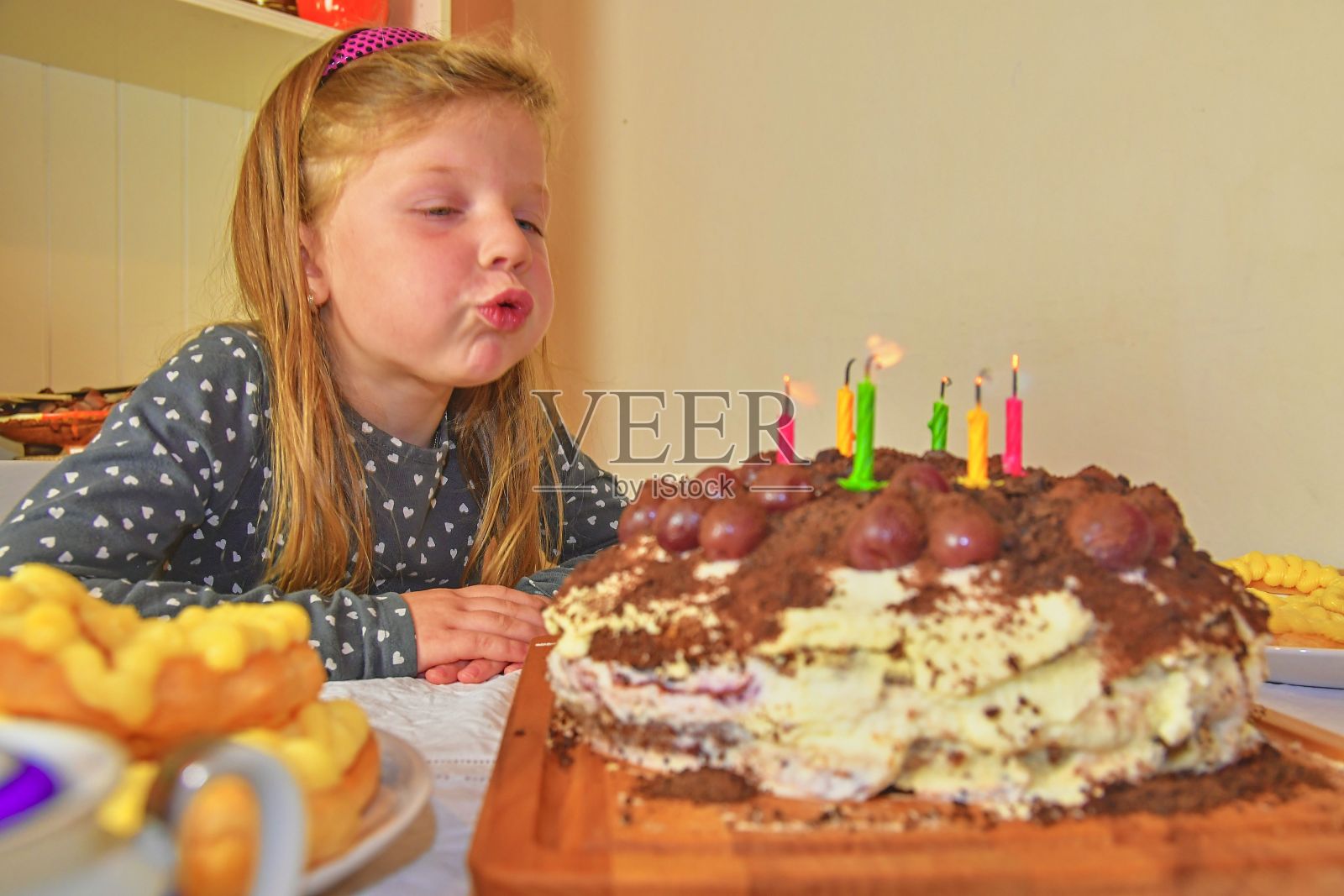 小女孩吹灭生日蛋糕上的蜡烛。小女孩庆祝她的六岁生日。生日蛋糕和小女孩照片摄影图片