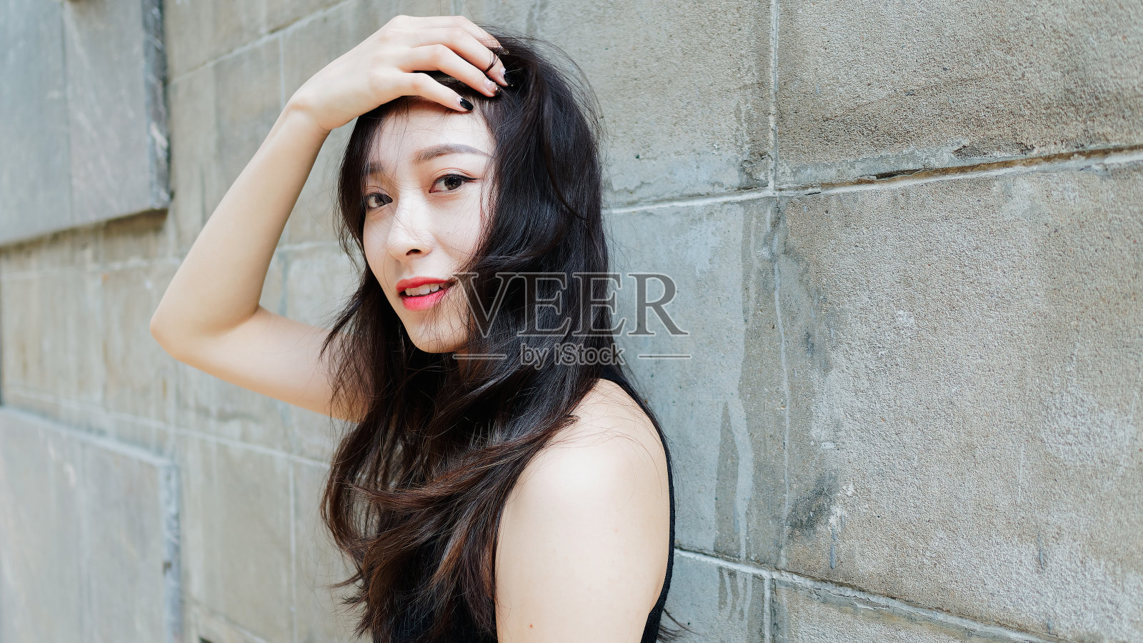 优雅的年轻女子与长长的黑发愉快地摆姿势与灰色的墙壁背景。室外特写照片酷中国女孩在时髦的夏天性感的黑色连衣裙。照片摄影图片