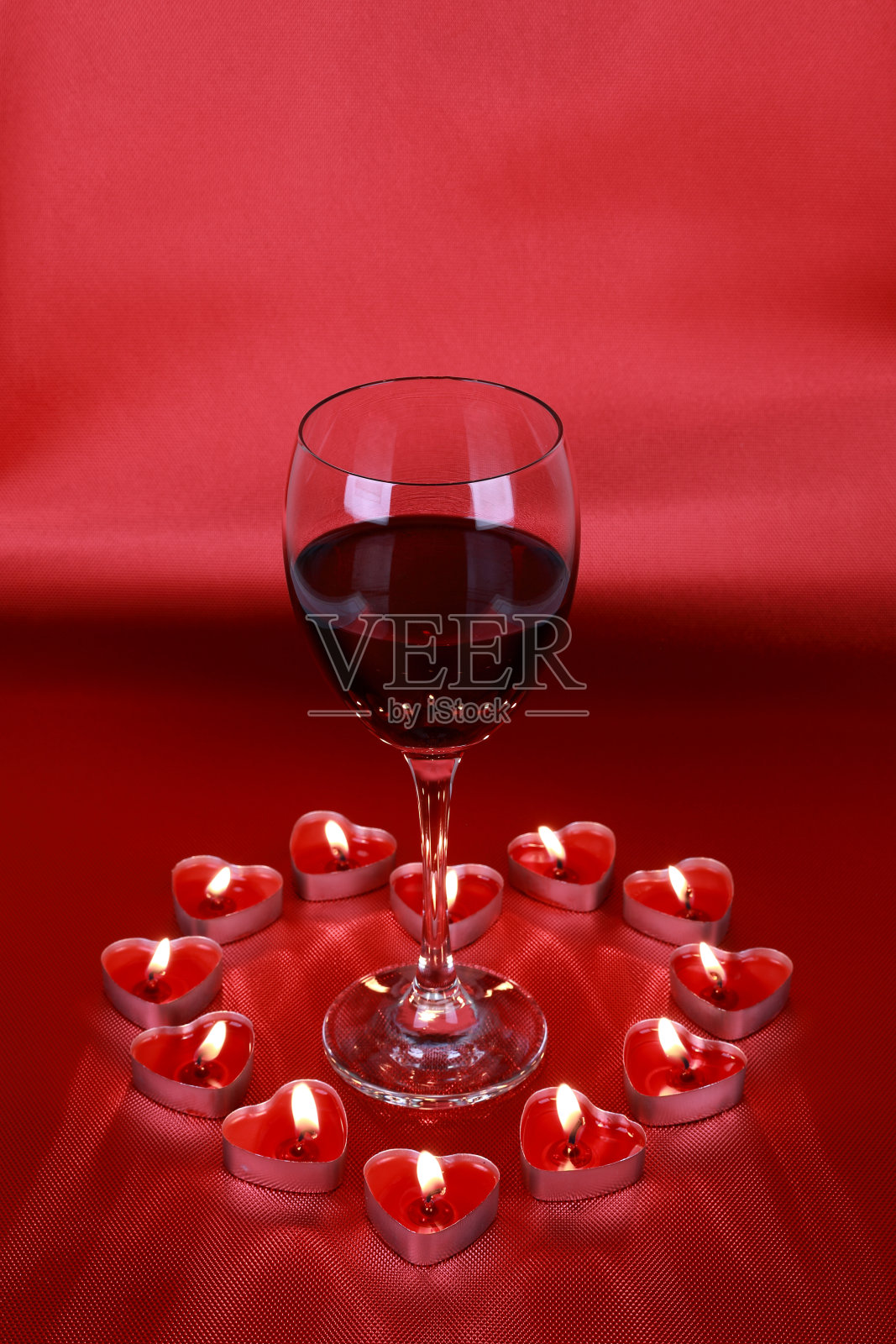 情人节，一杯红酒配上红色背景的心形蜡烛。照片摄影图片