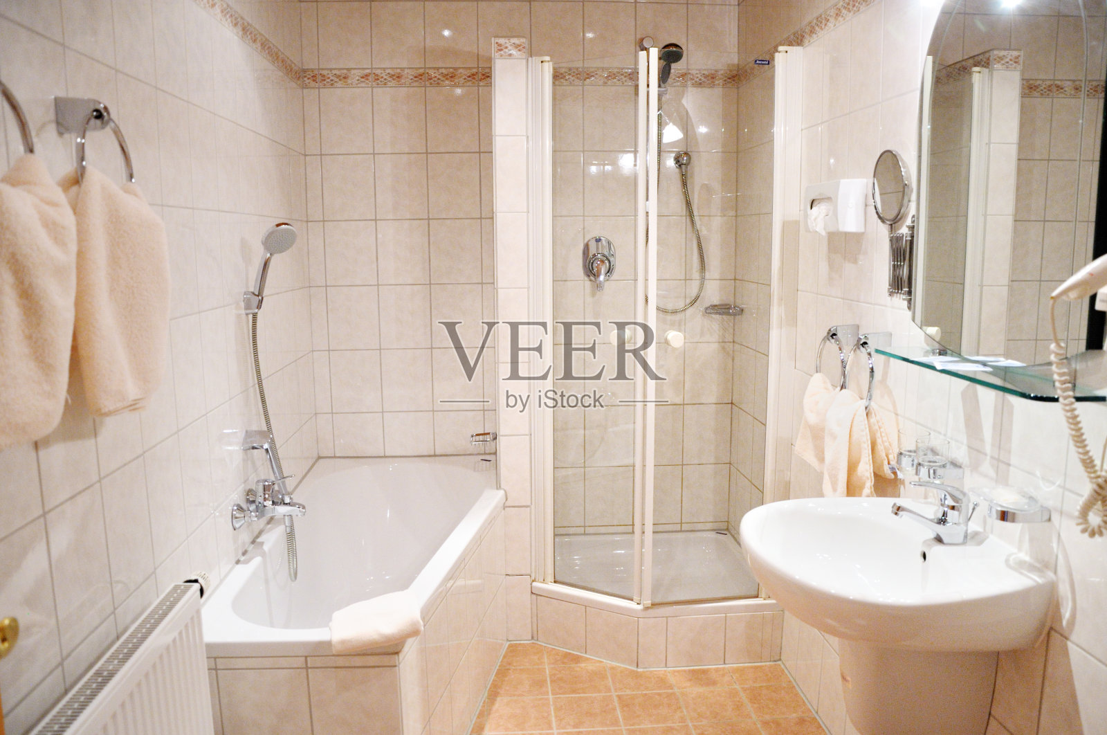 美丽宽敞明亮的浴室在酒店房间。明亮的瓷砖，白色的浴缸，淋浴，水槽，化妆镜，毛巾。照片摄影图片