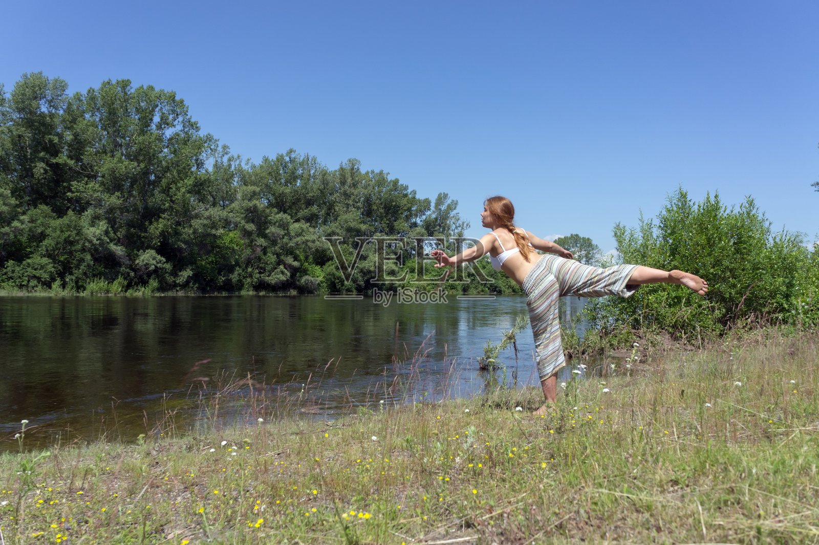 一个夏日阳光明媚的日子，红发女孩在河边的树林里做瑜伽。照片摄影图片
