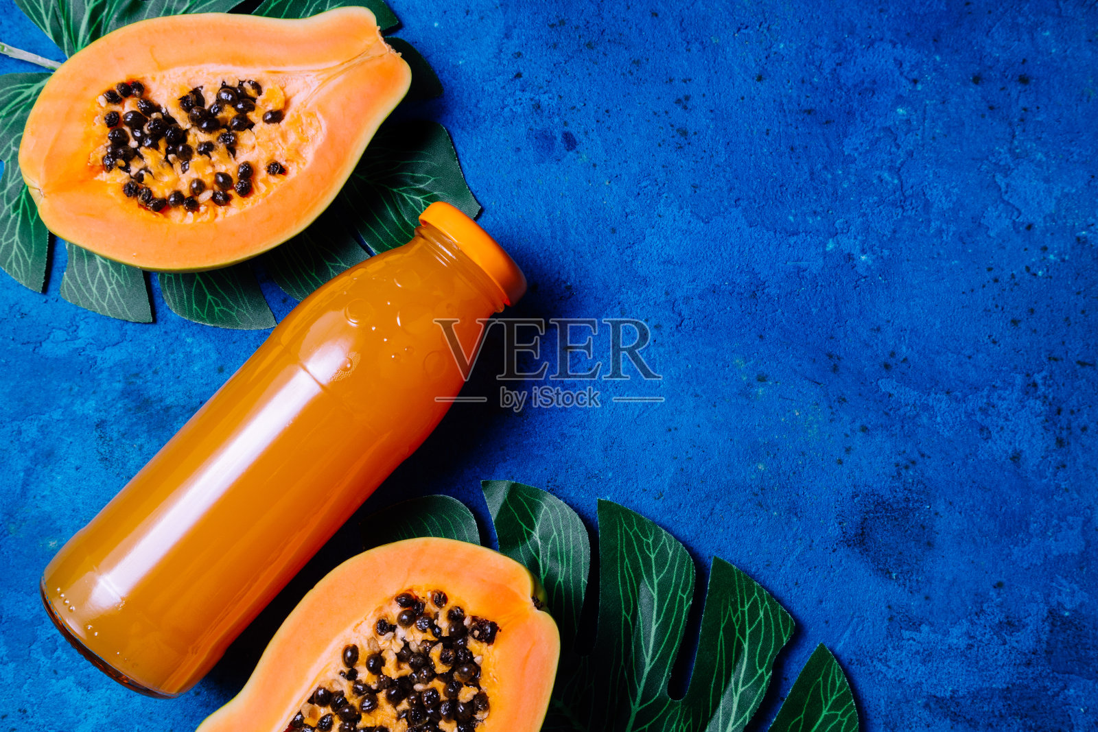夏季热带背景有异国情调的木瓜汁，绿色的棕榈叶上的蓝色。水果背景和夏季饮料。俯视图照片摄影图片