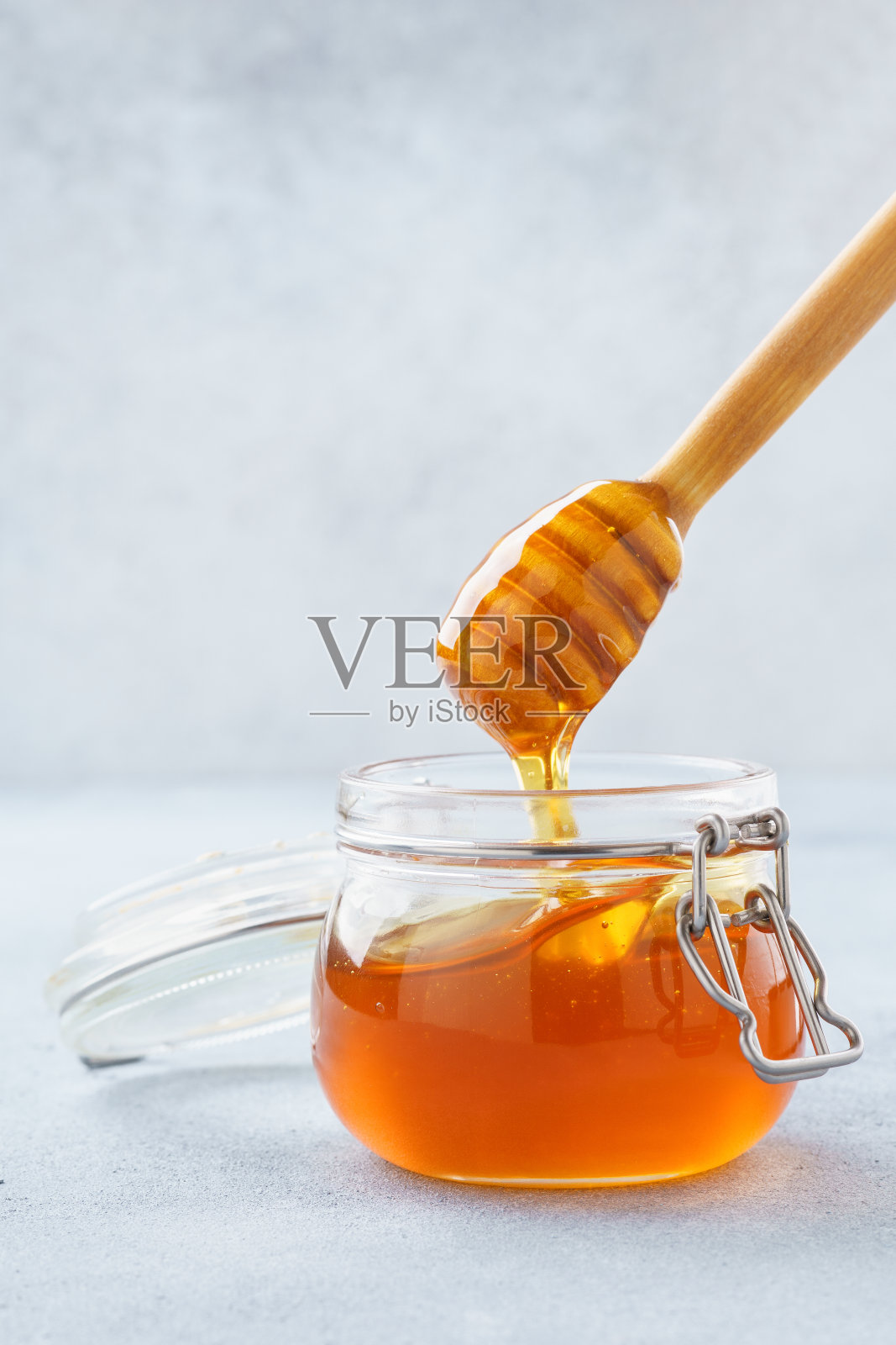 蜂蜜从木勺滴在罐子里。照片摄影图片