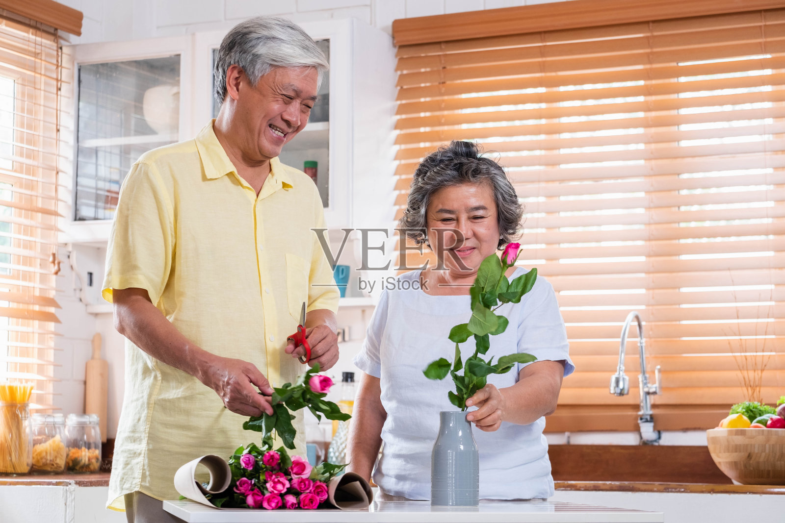 亚洲老两口夫妻在情人节将鲜花插花放在家里厨房桌上的花瓶上。可爱的老年夫妇概念。照片摄影图片