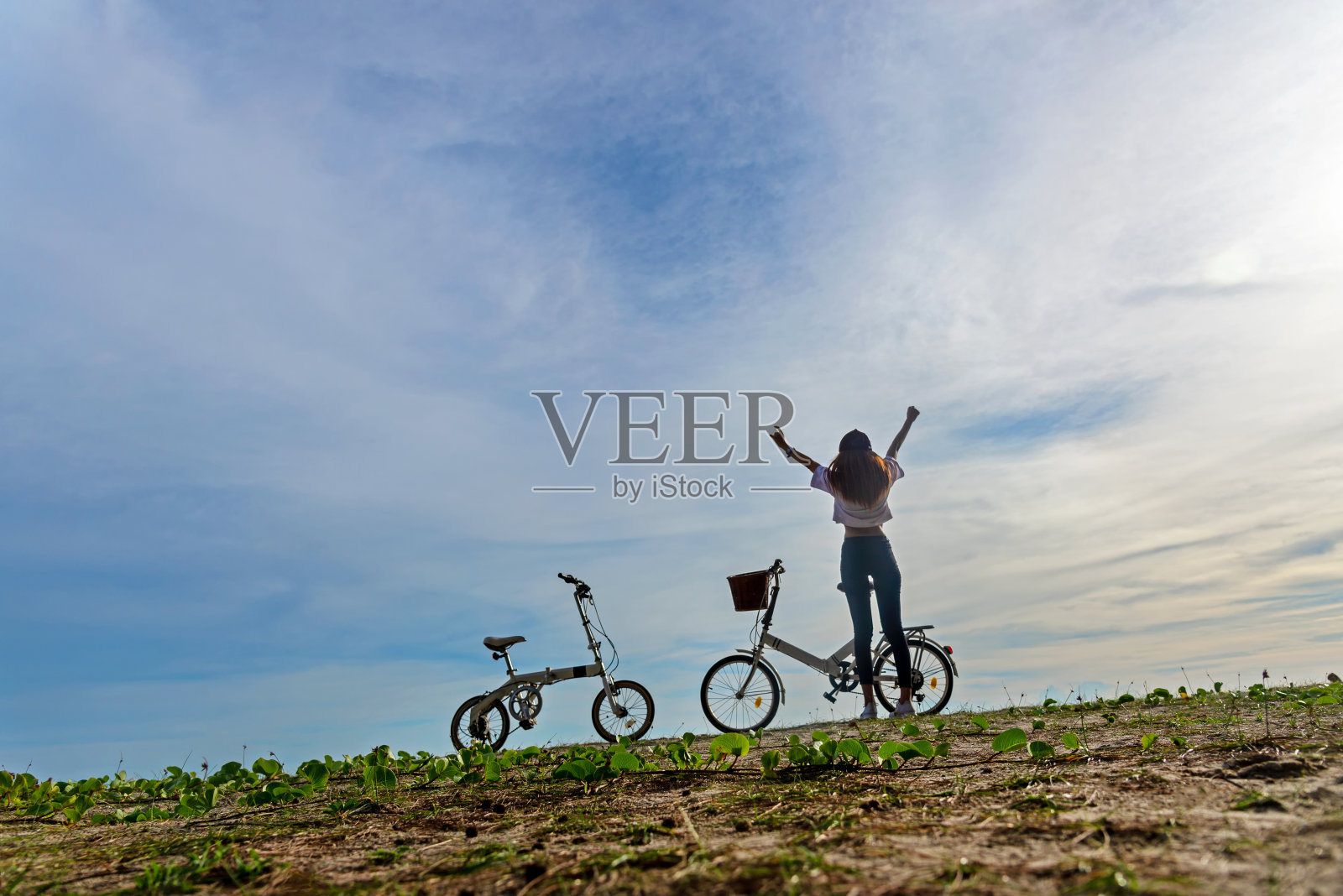 快乐无忧无虑的女人有乐趣骑自行车和举起她的胳膊在户外的海滩蓝天背景，放松和自由的假期夏季时间。夏季与旅游概念照片摄影图片