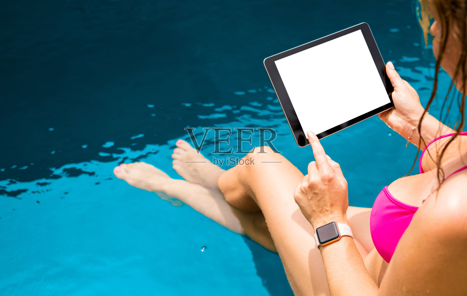 泳池边的女人水平地拿着平板电脑，上面有空白的模拟屏幕。照片摄影图片
