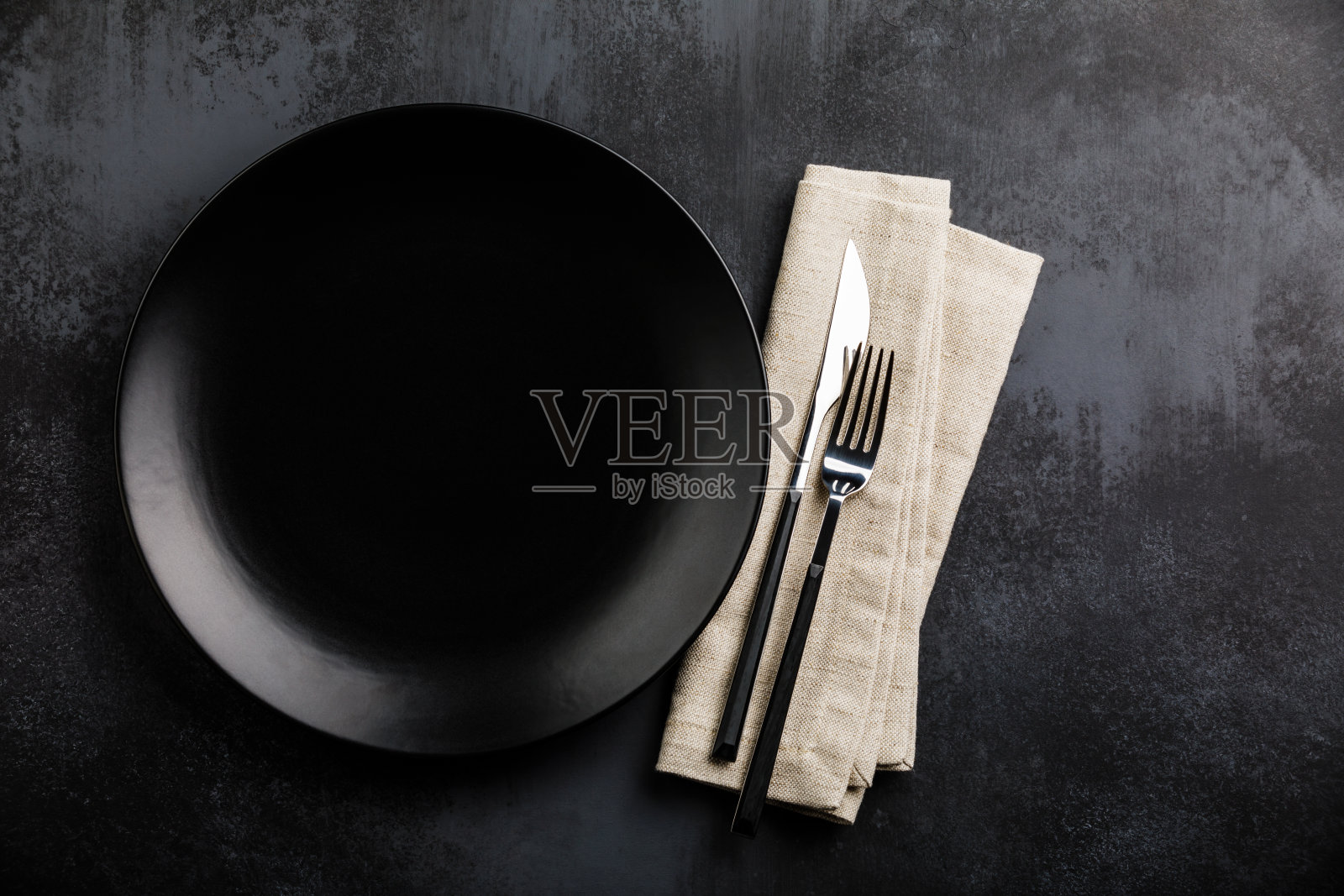 黑色的餐桌上摆放着黑色的空盘子、刀叉和亚麻餐巾照片摄影图片