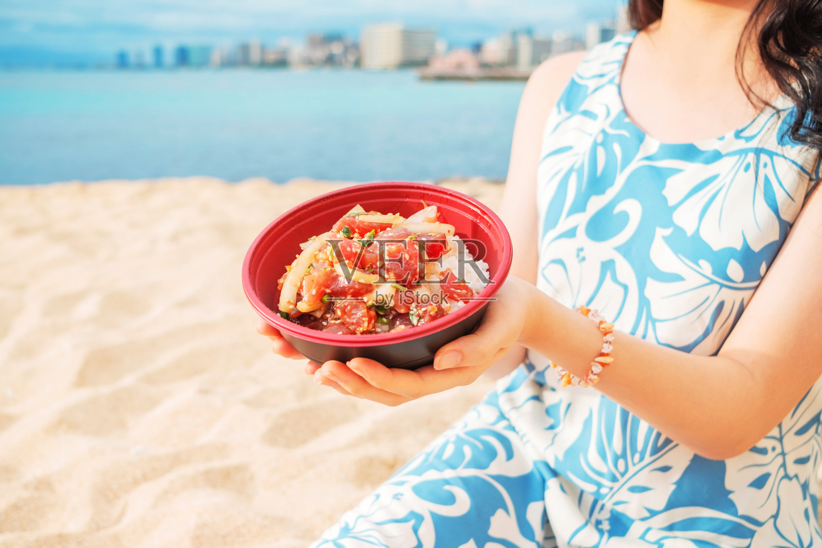 一个女孩坐在怀基基海滩上，拿着夏威夷Ahi Poke碗照片摄影图片