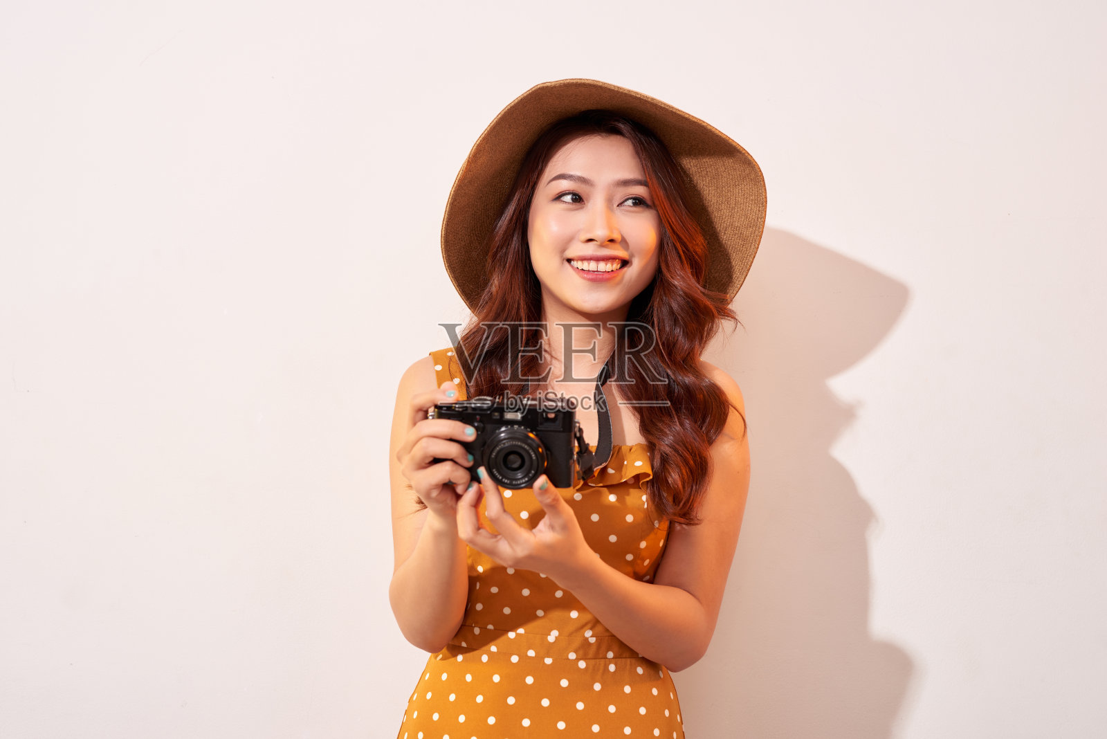 肖像的快乐微笑的年轻女子拍照与灵感和穿着夏天的连衣裙。拿着复古相机的女孩。模特在米色背景在帽子摆姿势照片摄影图片