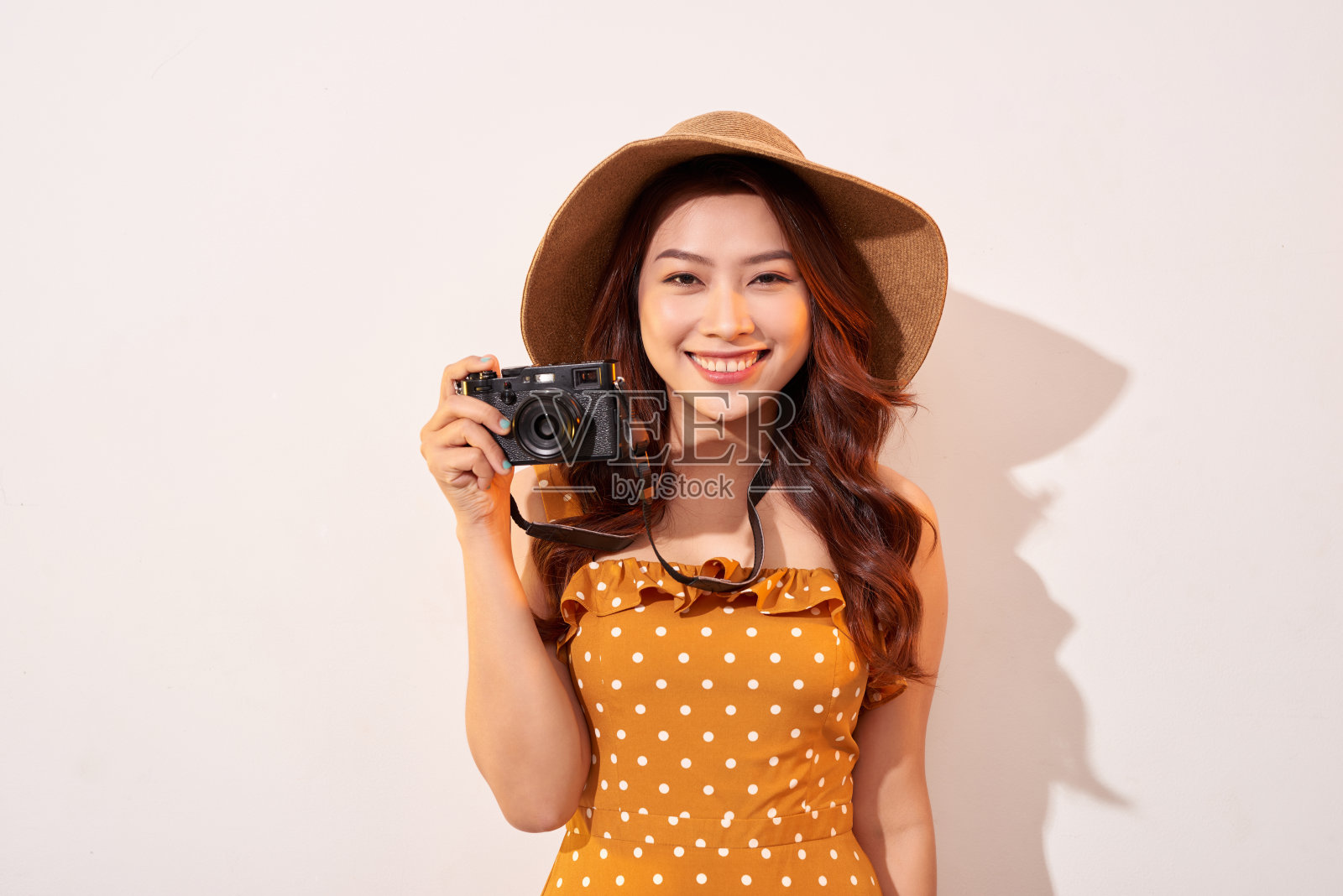 肖像的快乐微笑的年轻女子拍照与灵感和穿着夏天的连衣裙。拿着复古相机的女孩。模特在米色背景在帽子摆姿势照片摄影图片