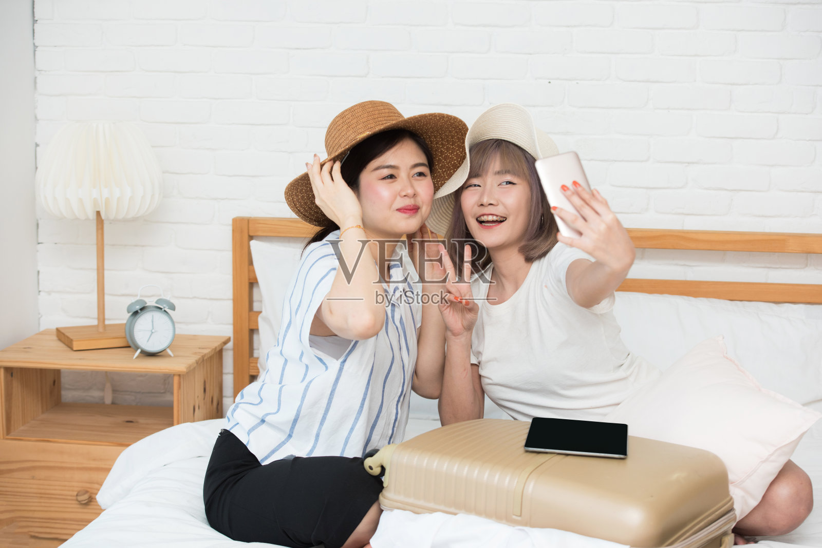 肖像两个亚洲快乐美丽的年轻女孩在床上自拍后完成网上订票旅行。照片摄影图片