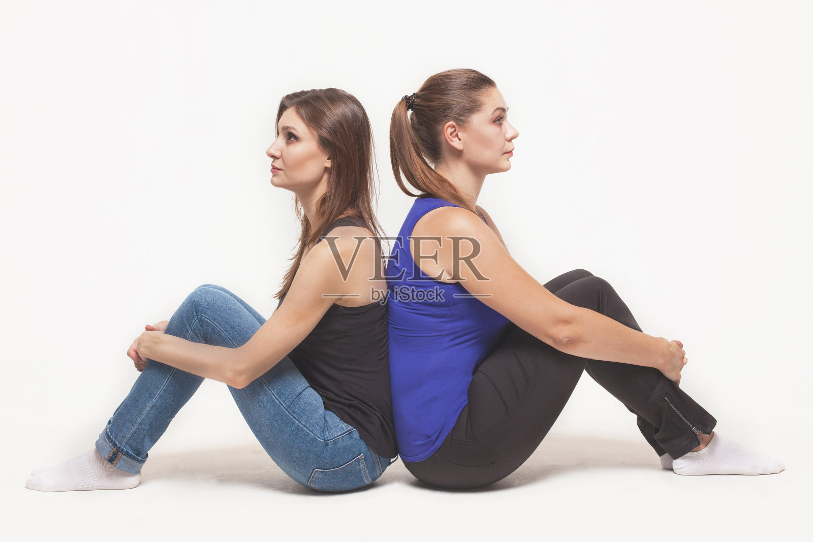 两个深色头发的年轻白人女性背靠背坐在地板上，抱着膝盖照片摄影图片