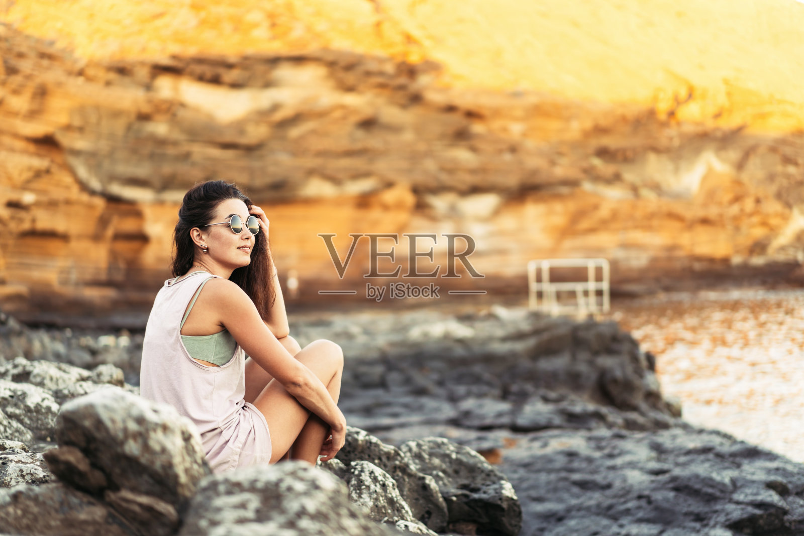 漂亮的长发黑发的女游客在海边的石头上休息。照片摄影图片