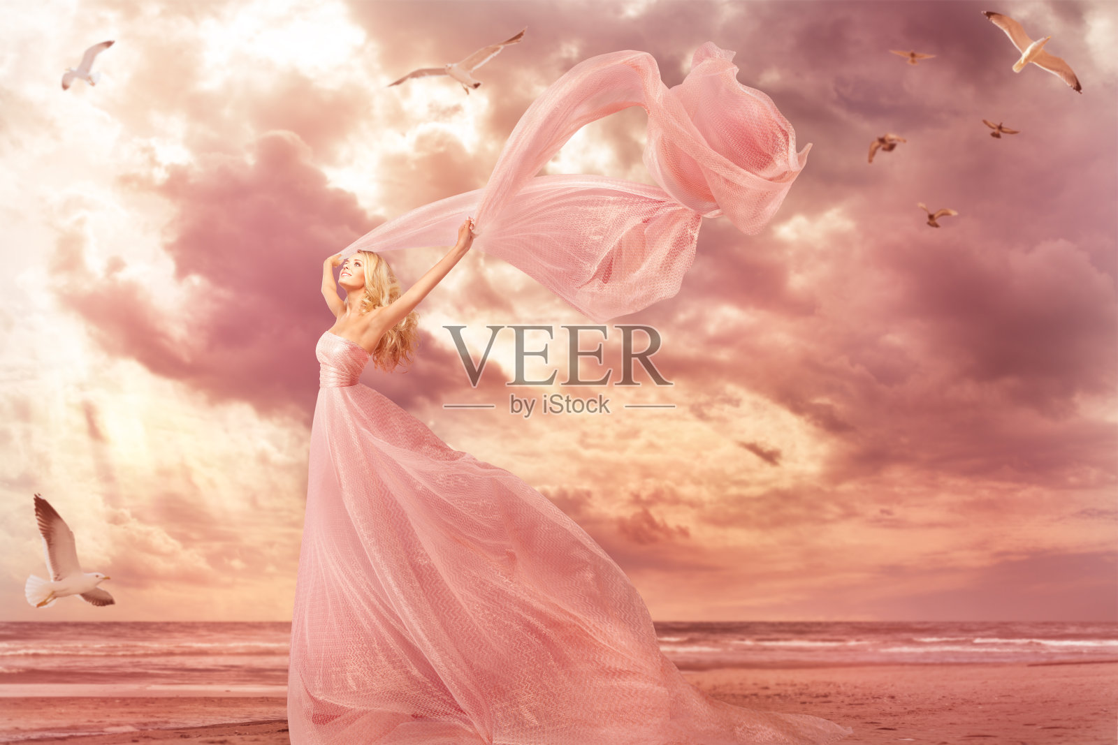 在海边穿着长裙的女人肖像，幻想女孩粉红色礼服与在暴风雨中飞翔的披肩照片摄影图片