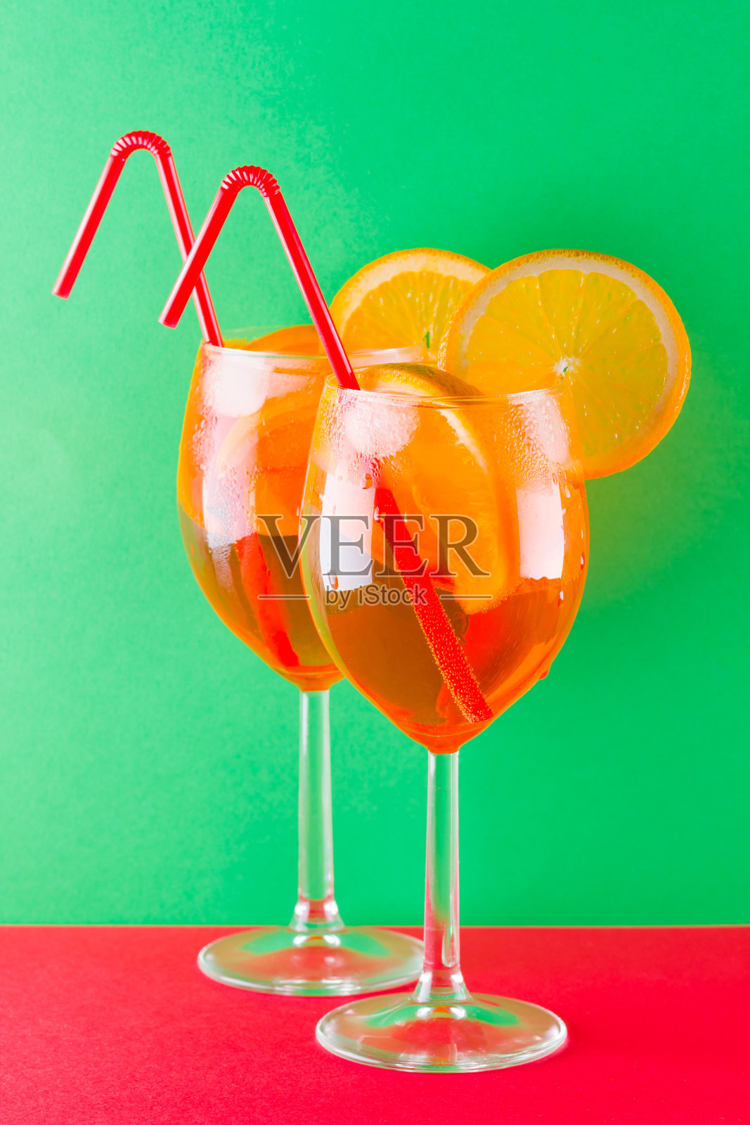 鸡尾酒喷在红绿背景上。夏日酒精鸡尾酒配橙子片。喷上彩色背景。极简主义风格的珊瑚色鸡尾酒照片摄影图片