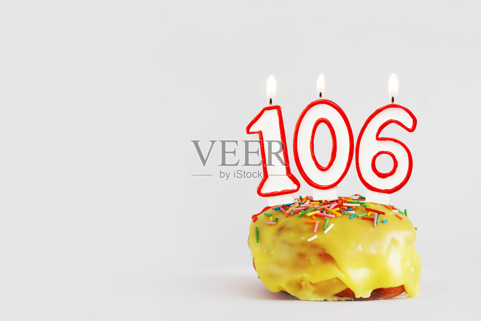 一百零六年的纪念日。生日纸杯蛋糕，白色燃烧的蜡烛和红色的边界在106数字的形式。浅灰色背景与复制空间照片摄影图片
