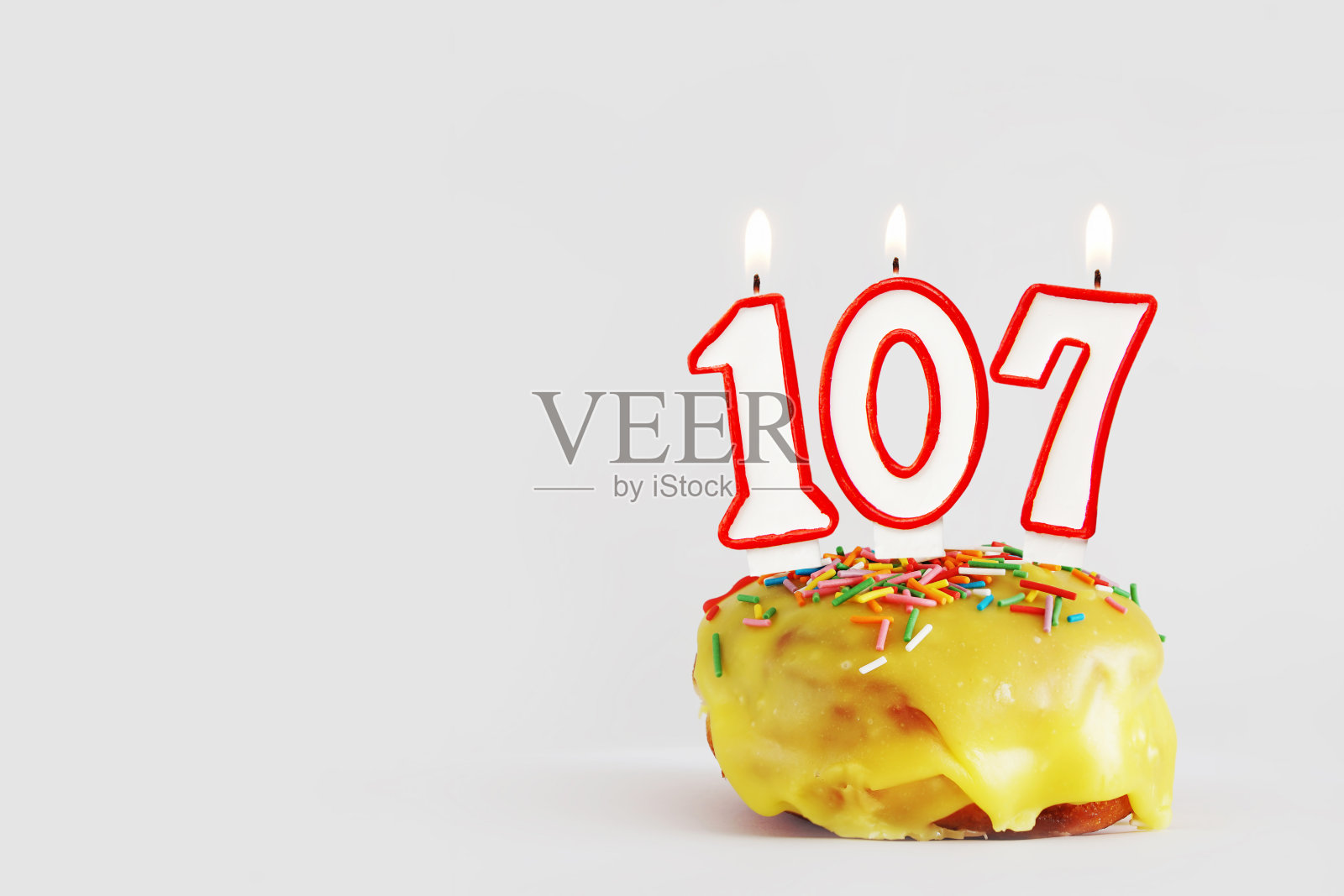 一百零七年的纪念日。生日纸杯蛋糕与白色燃烧的蜡烛与红色边框形式的107数字。浅灰色背景与复制空间照片摄影图片