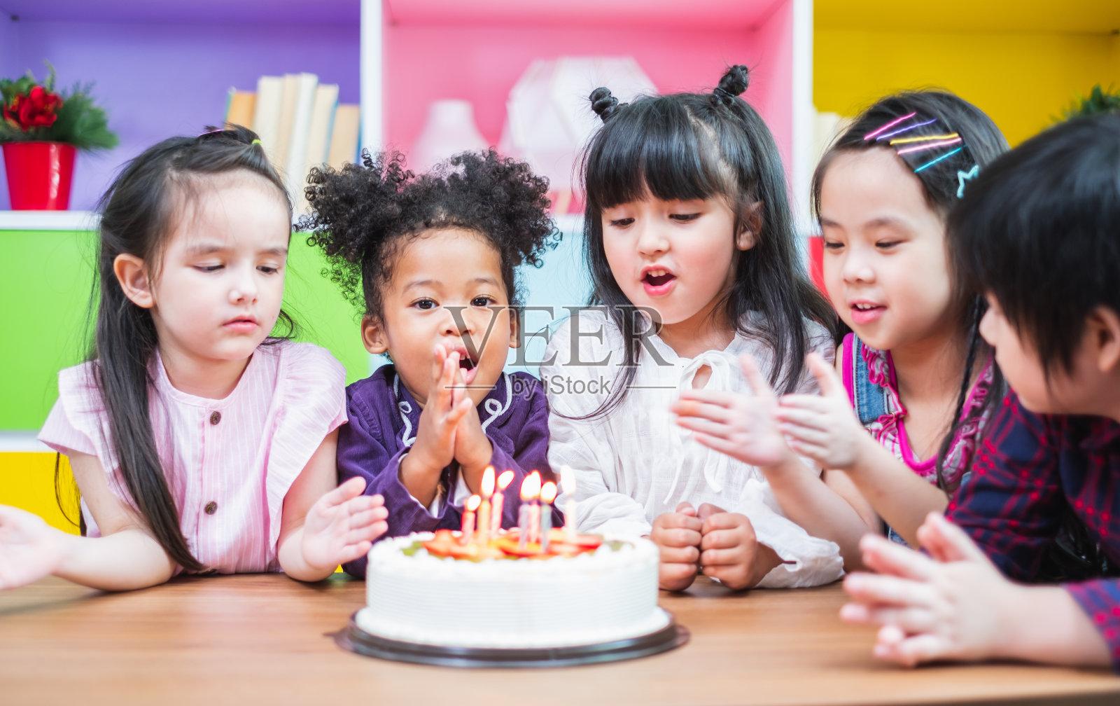 团体多元化的孩子吹生日蛋糕。照片摄影图片
