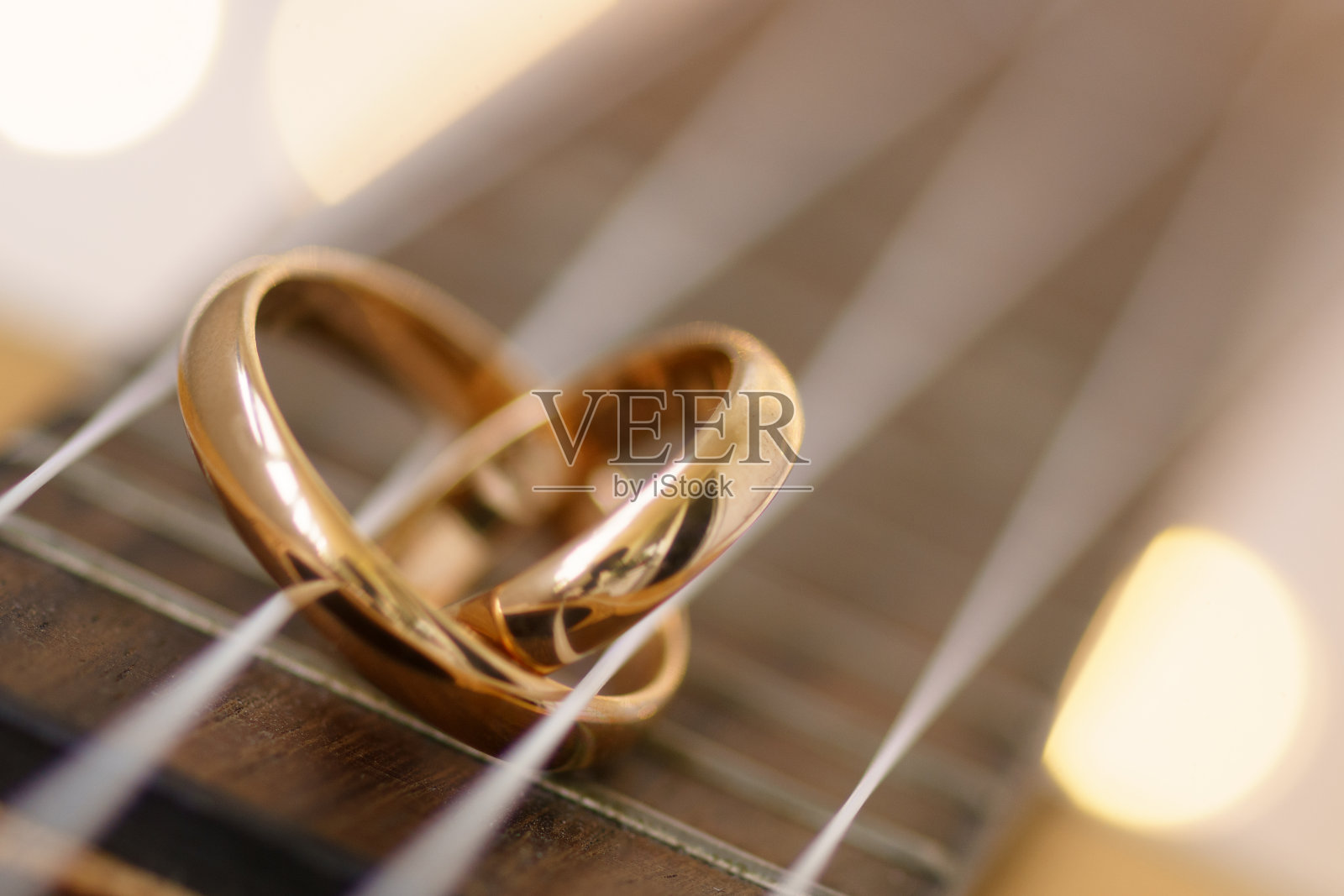 在尤克里里吉他弦上的心形结婚戒指。照片摄影图片