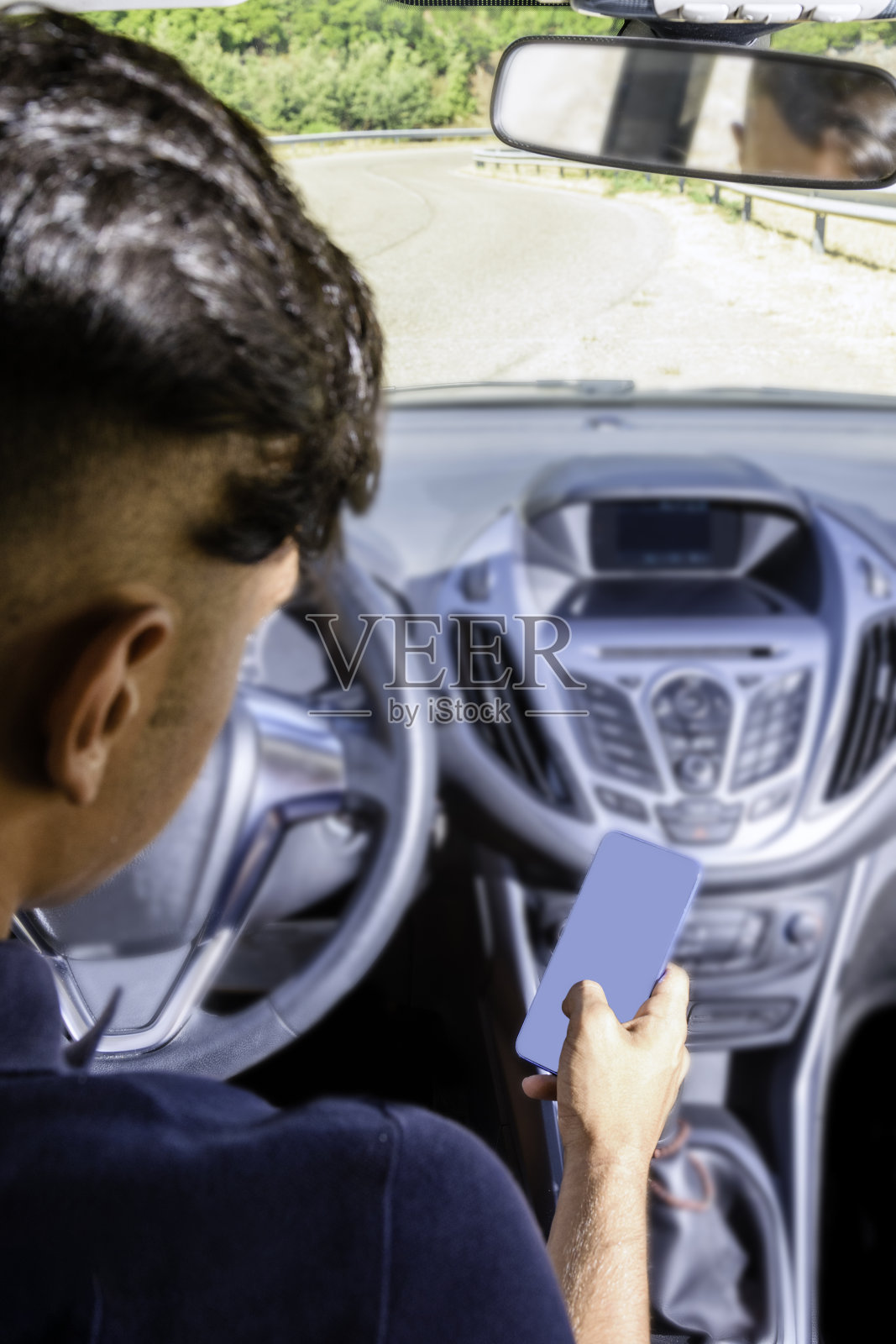 年轻的司机，用智能手机，在路上开车。照片摄影图片