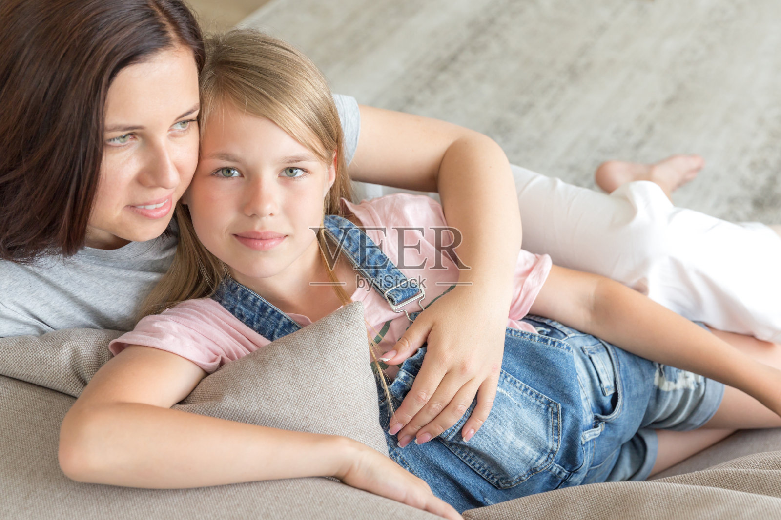 母亲和十来岁的女儿坐在沙发上微笑。幸福的家庭的概念照片摄影图片