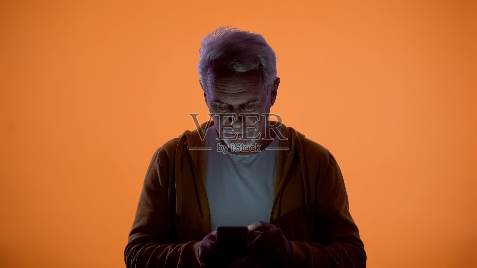 心烦意乱的老人在智能手机上输入信息，橙色的背景，视力问题照片摄影图片