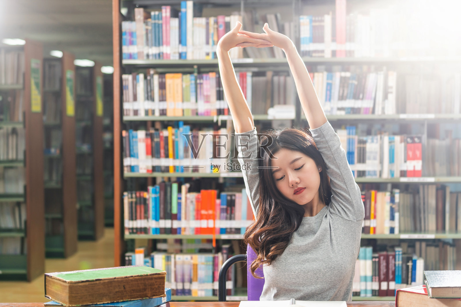 亚洲青年学生穿着休闲服在大学或学院的图书馆里读书、伸展，书架上方的木桌上放着各种书籍和文具，回到学校照片摄影图片